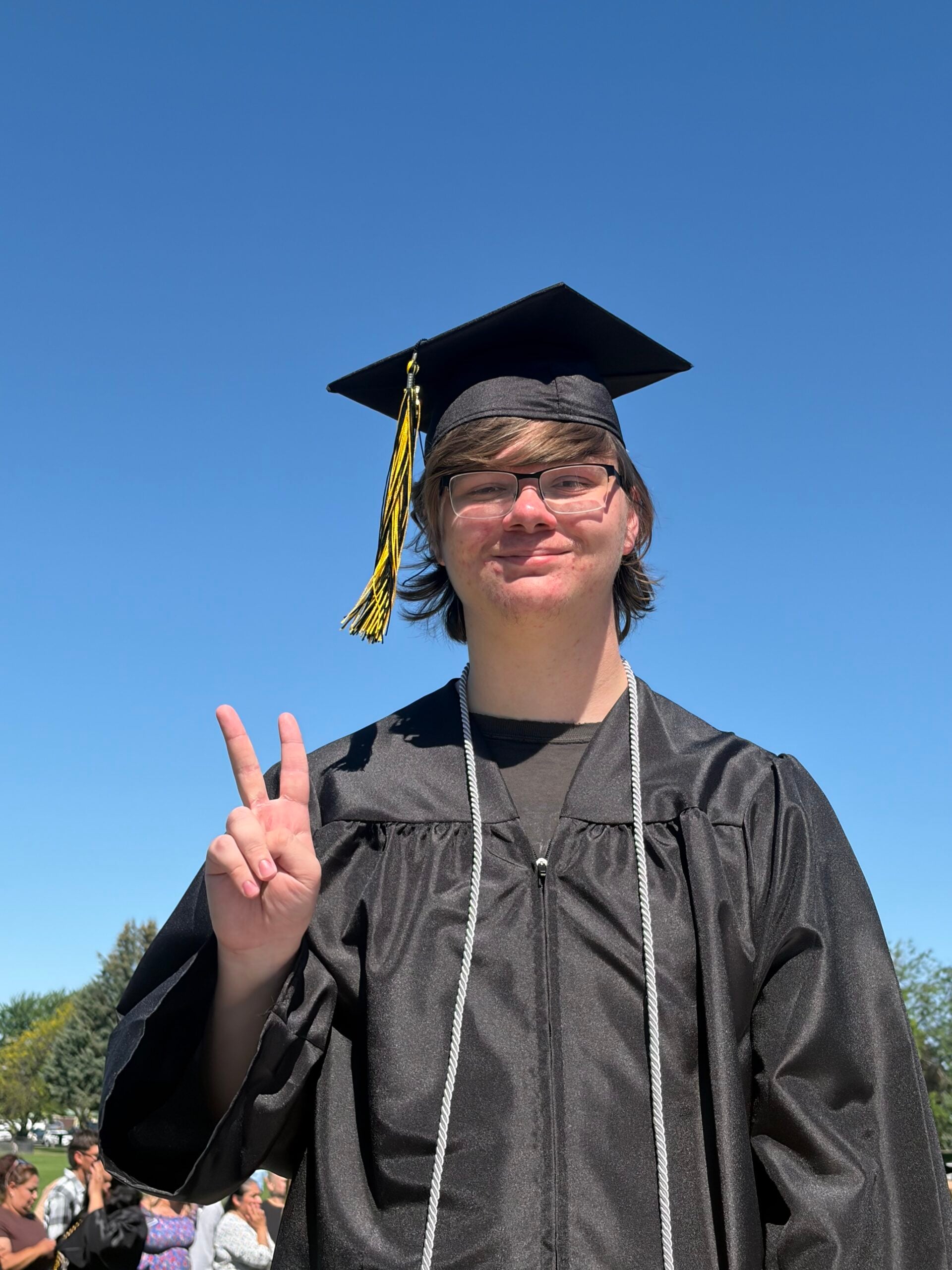 Audio engineering graduate in cap and gown standing at a WWCC commencement ceremony with fellow graduates in the background.