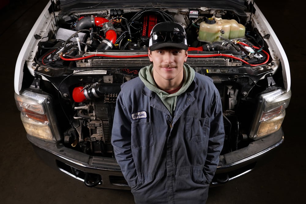Student standing in front of a truck engine that he worked on.