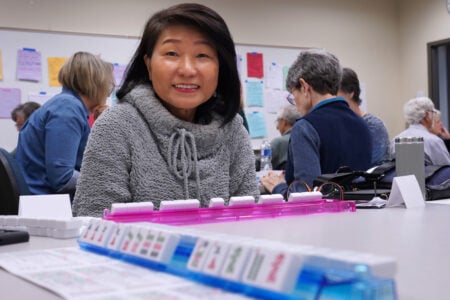 Adult student smiling while playing a classroom game activity with other students in the background.