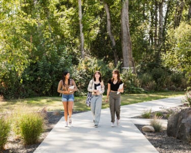 Running Start students carrying books walking on the sidewalk outside the Main Building D Science Wing