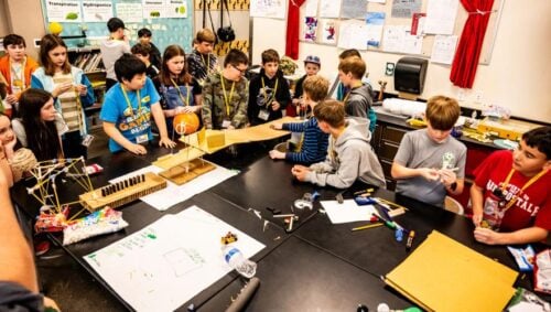 Children at one of the Kids College sessions gather on Thursday, April 9, to see whether one team's construction will succeed by rolling a marble down the contraption to knock a wad of paper into a trash can.