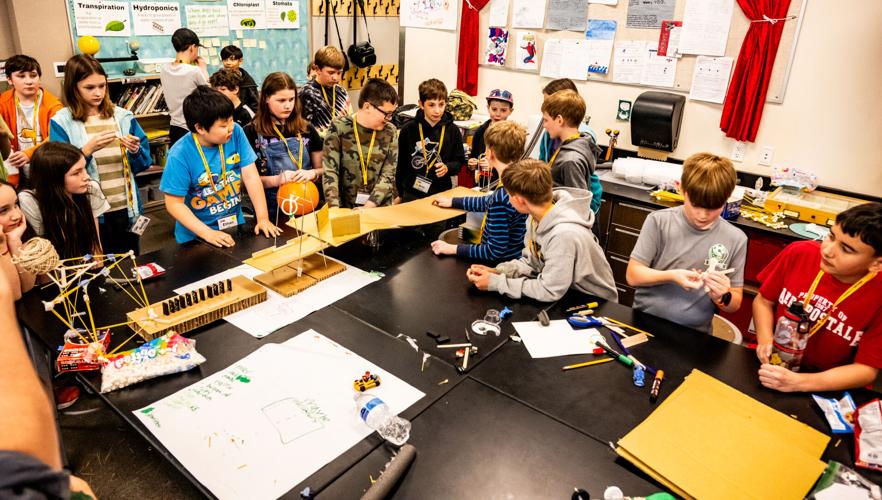 Children at one of the Kids College sessions gather on Thursday, April 9, to see whether one team's construction will succeed by rolling a marble down the contraption to knock a wad of paper into a trash can.